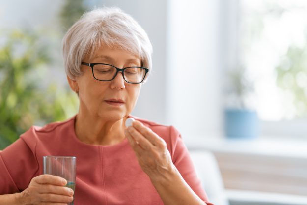 woman holding pill and glass of fresh water