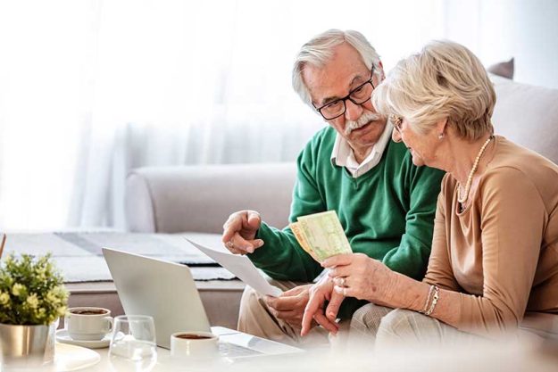 Senior couple sitting at a table at home and going through their household finances using a laptop Senior couple sitting at a table at home and going through their household finances using a laptop