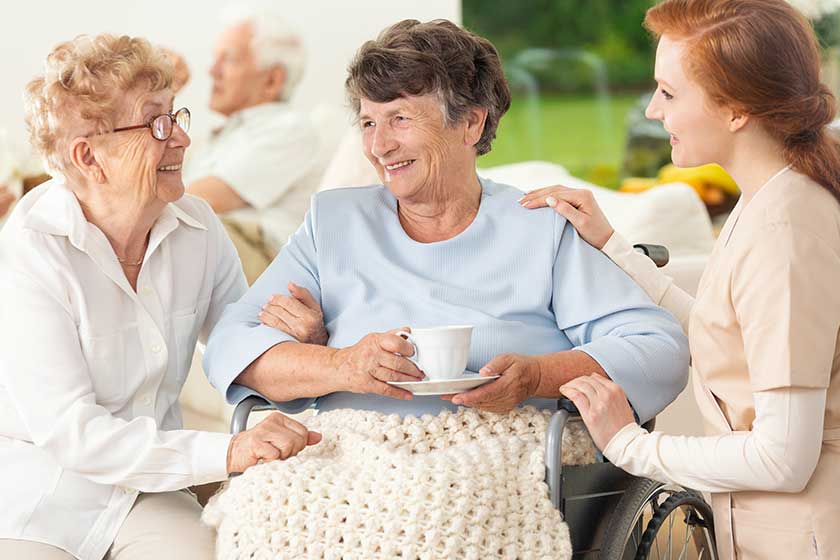 Smiling paralysed senior woman between happy friend and nurse