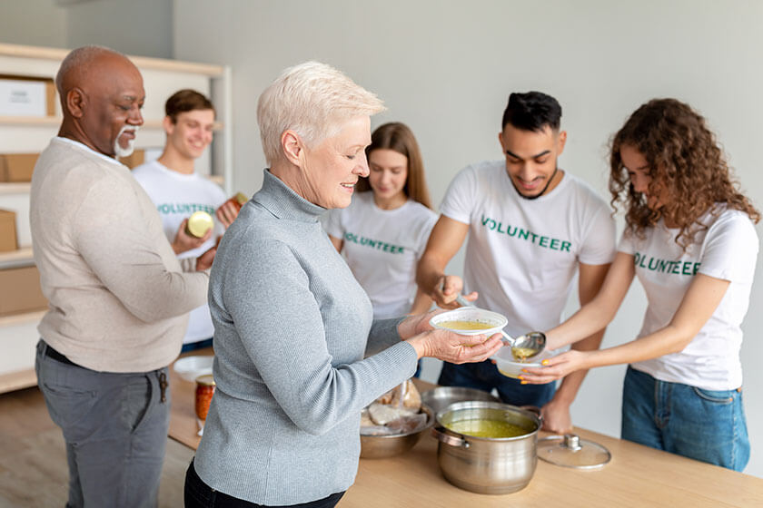 Happy senior woman received warm soup in charity organization office