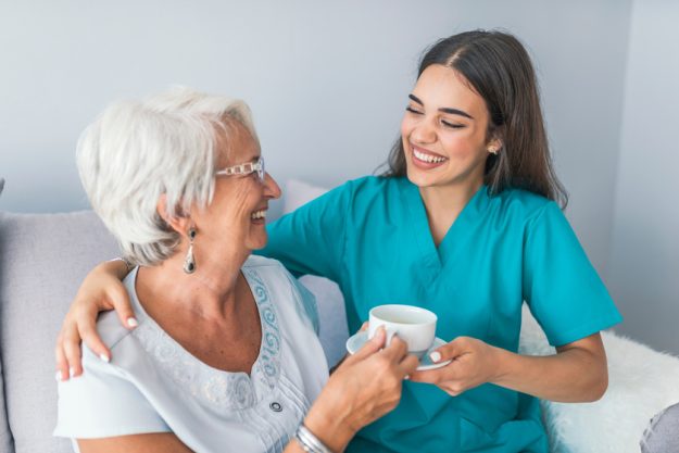 Happy senior woman talking with friendly nurse at geriatric ward