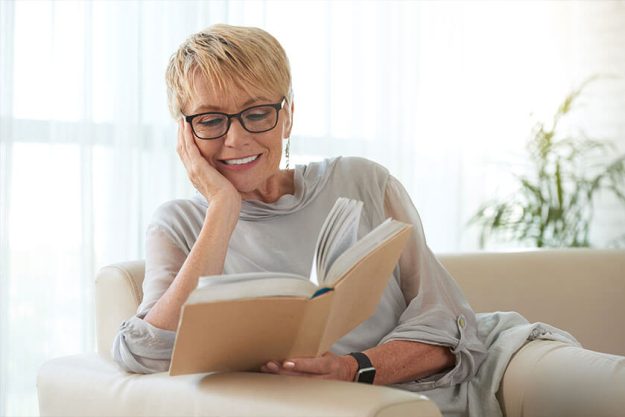 Senior blond woman in glasses resting on sofa and reading a book Senior blond woman in glasses resting on sofa and reading a book