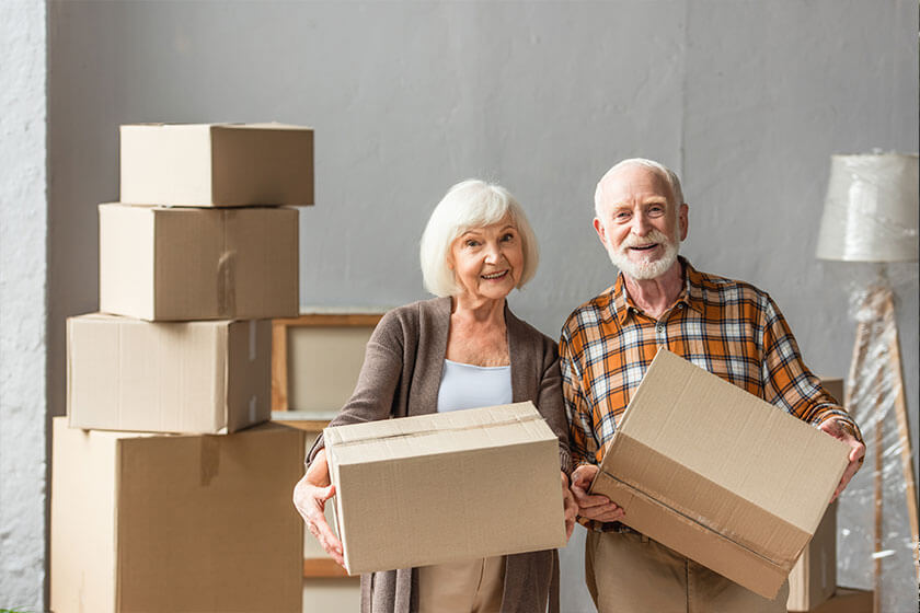 senior couple holding cardboard boxes and looking at camera in new house senior couple holding cardboard boxes and looking at camera in new house
