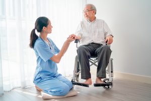 Asian nurse or doctor sit on floor and hold hands of senior man