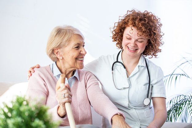 Young caregiver and senior woman laughing together while sitting on sofa Young caregiver and senior woman laughing together while sitting on sofa