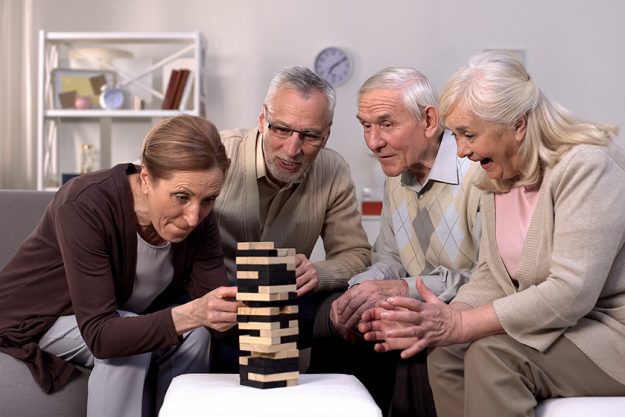 Elderly friends building tower from wooden cubes leisure time in nursing home