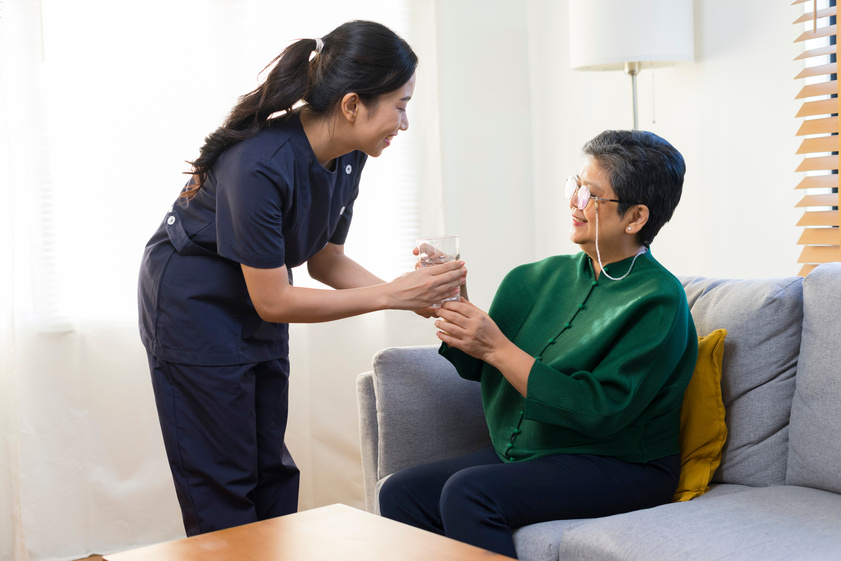Smiling nurse giving glass of water to senior asian woman in nur Smiling nurse giving glass of water to senior asian woman in nur