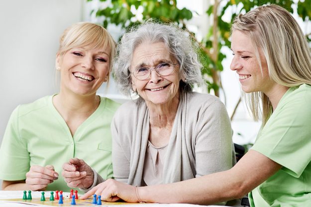 Senior woman playing a board game with nurses Senior woman playing a board game with nurses