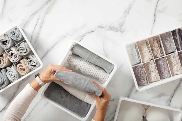 Woman hands neatly folding underwears and sorting in drawer organizers on white marble background Woman hands neatly folding underwears and sorting in drawer organizers on white marble background