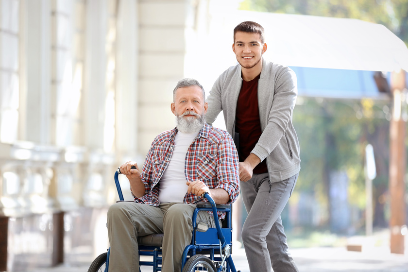 Young caregiver walking with senior man, outdoors