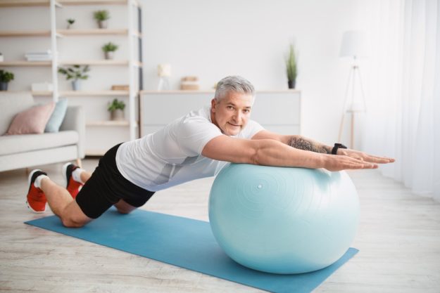 Home workout concept. Athletic senior man exercising with fitness ball, working out core muscles at home Home workout concept. Athletic senior man exercising with fitness ball, working out core muscles at home