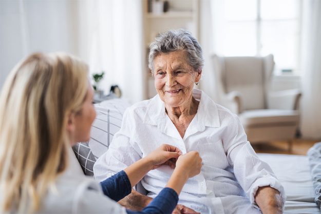 A health visitor helping a sick senior woman sitting on bed at home A health visitor helping a sick senior woman sitting on bed at home