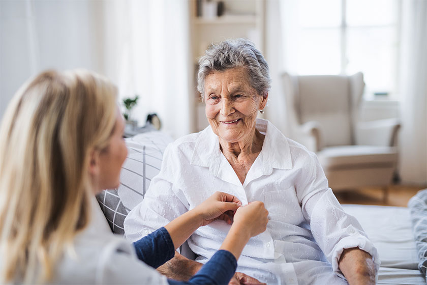 A health visitor helping a sick senior woman sitting on bed at home A health visitor helping a sick senior woman sitting on bed at home