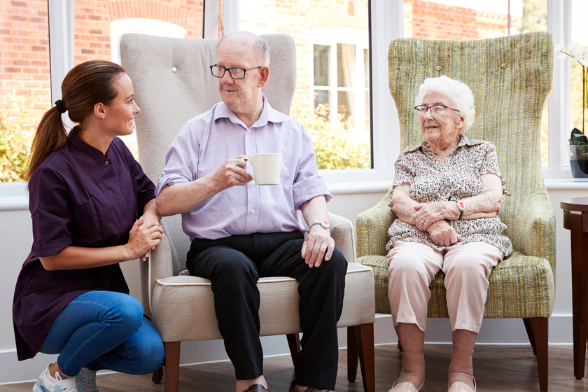 Male And Female Residents Sitting In Chair And Talking With Carer In Retirement Home CCRC Vs. Independent Living Community In Sublett, TX: Choosing The Best Option
