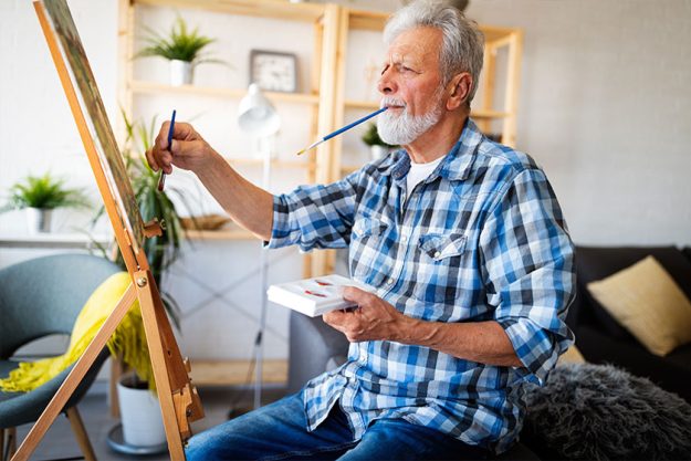 Smiling mature man painting on canvas at home Smiling mature man painting on canvas at home