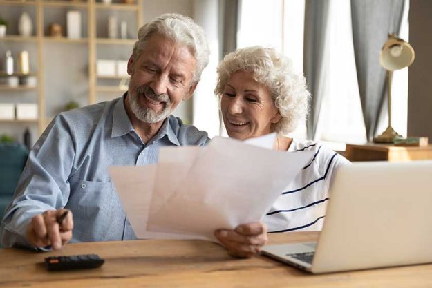 Happy older mature family couple enjoying calculating domestic expenses or planning monthly budget together Happy older mature family couple enjoying calculating domestic expenses or planning monthly budget together