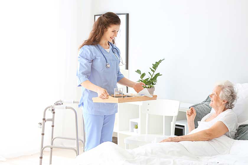 Young caregiver bringing senior woman breakfast in bed