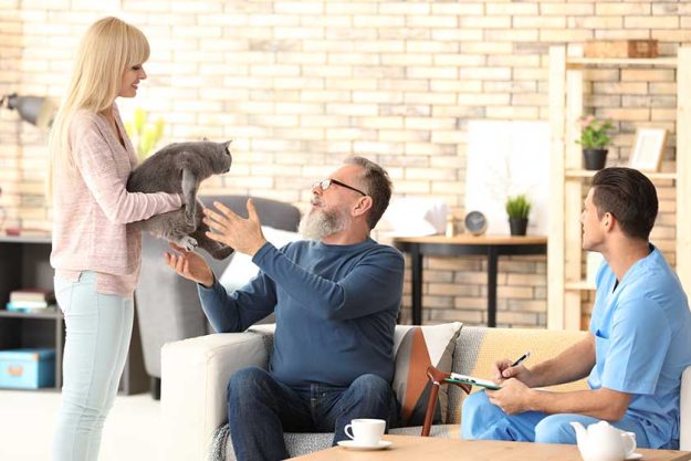 Daughter giving cute cat to her senior father at home