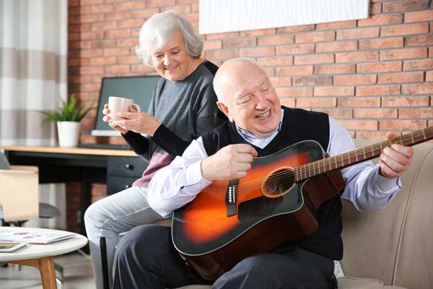 Elderly man playing guitar for his wife on sofa