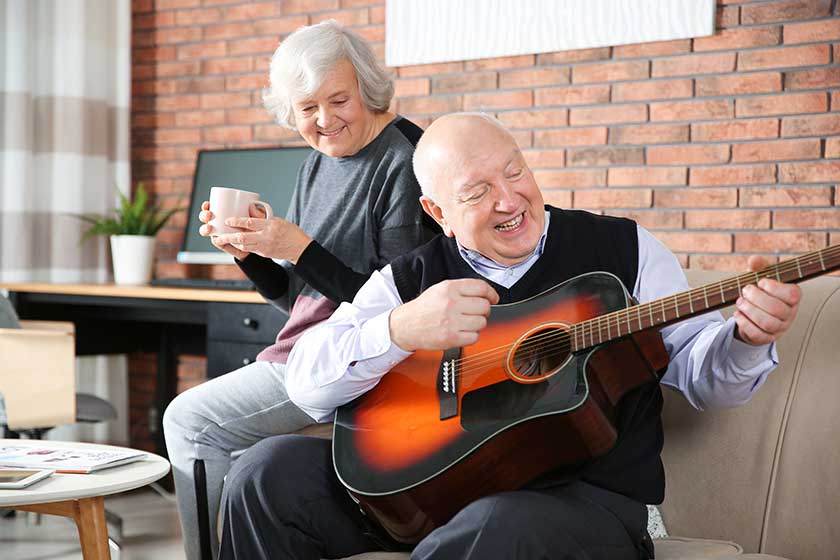 Elderly man playing guitar for his wife on sofa