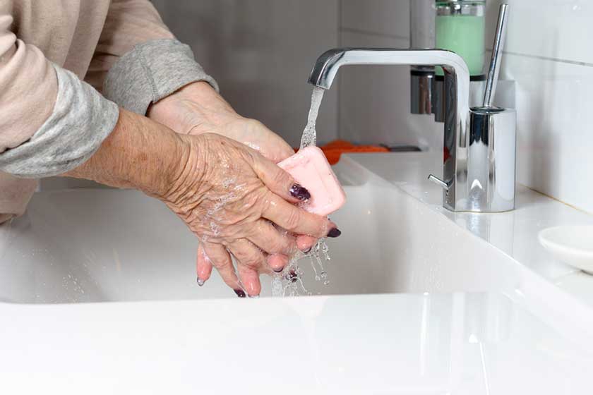 Elderly woman washing hands under tap Elderly woman washing hands under tap