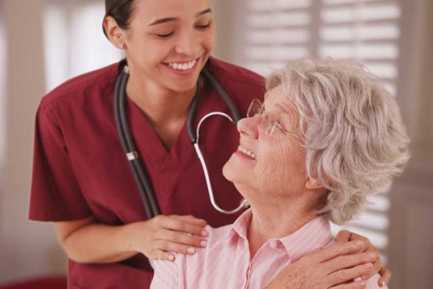 Hispanic female nurse looking and smiling with senior Hispanic female nurse looking and smiling with senior