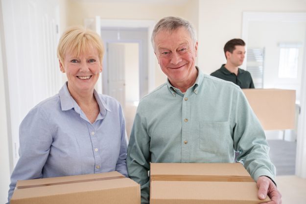 Portrait Of Senior Couple Downsizing In Retirement Carrying Boxes