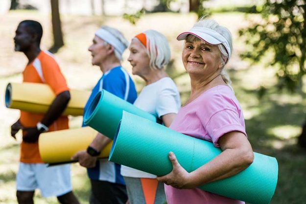 Selective Focus Happy Retired Woman Cap Holding Fitness Mat Multicultural
