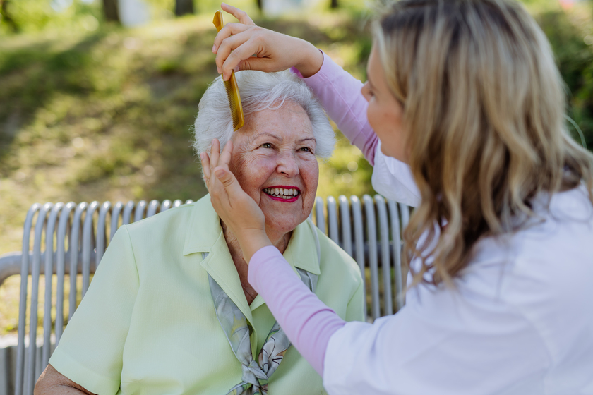 Caregiver helping senior woman to comb hair and make hairstyle when sitting on bench in park in summer. What Is The Best Season To Consider An Independent Living Home Care In Bisbee, TX?
