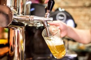 Barman hand at beer tap pouring a draught lager beer serving in a restaurant