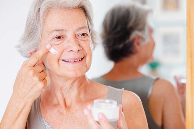 senior beautiful woman applies anti aging cream on wrinkled face