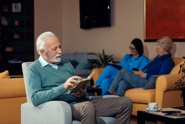 Smiling senior man siting in nursing home reading a book Smiling senior man siting in nursing home reading a book