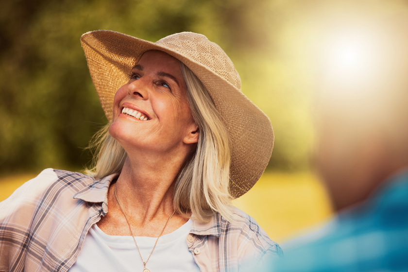 Smiling senior woman enjoying a wine tasting day on a farm with friends. Happy caucasian woman wearing a hat while sitting and bonding on a vineyard. Elderly woman on a wine farm during the weekend Smiling