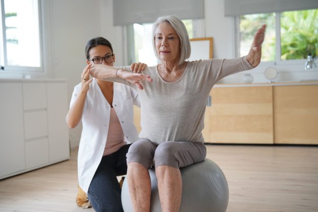 Senior woman exercising with her physiotherapist and swiss ball A Skilled Nursing And Rehab Community In Little River, TX Can Help Senior Manage Their Depression Symptoms