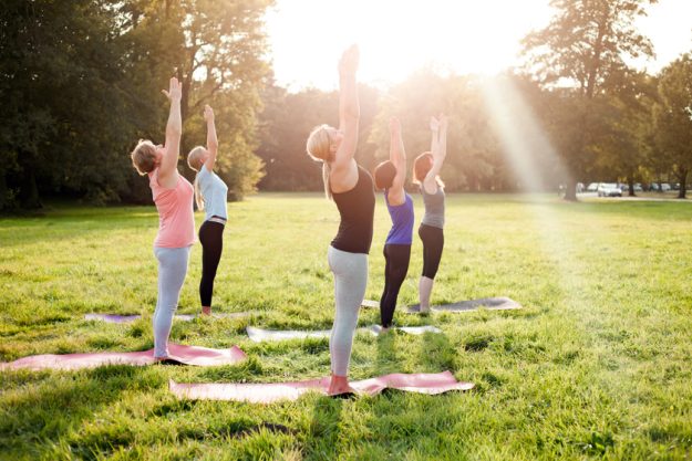Mixed age group of people practicing yoga outside in the park while sunset Embrace A Maintenance-Free Lifestyle With Continuing Care Retirement Communities In Hughes, TX