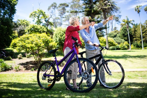 Senior couple standing with bicycle in park on a sunny day Free & Low-Cost Spring Activities To Do When Staying At Senior Living Properties In Baytown, TX