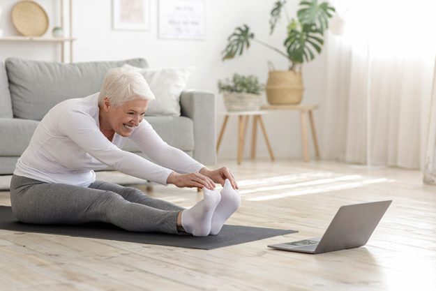 Active Senior Woman Doing Warming Stretching Exercises In Front Of Laptop