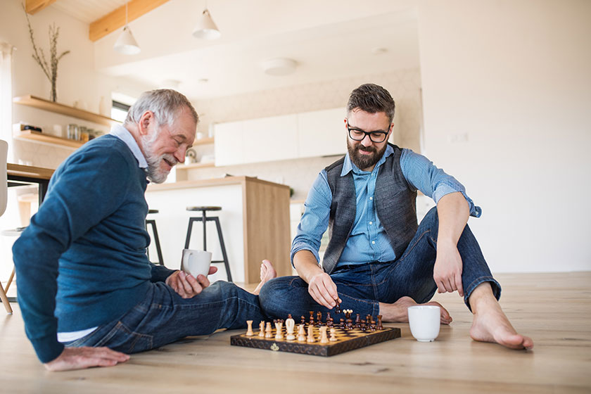 An adult hipster son and senior father sitting on floor