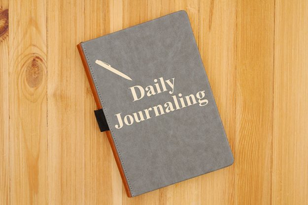 Daily journaling message with a pen icon written on a journal on a wood desk