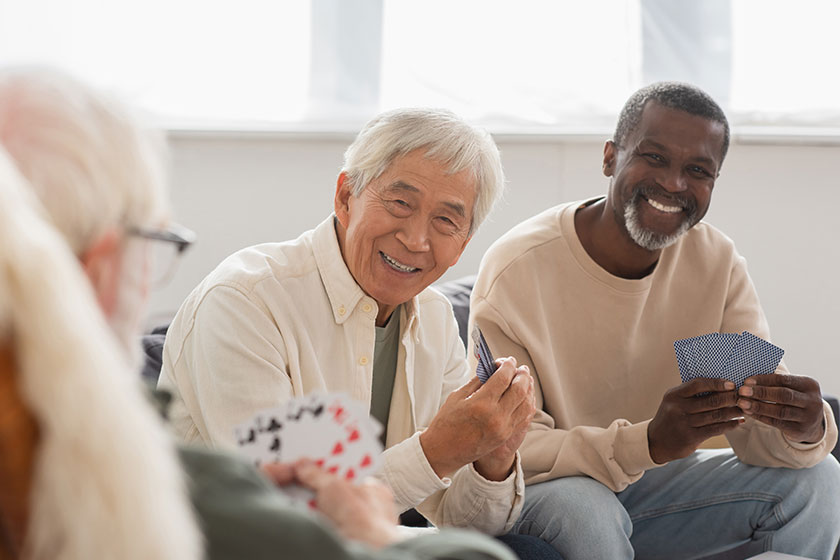 Elderly multiethnic men playing cards with blurred friend