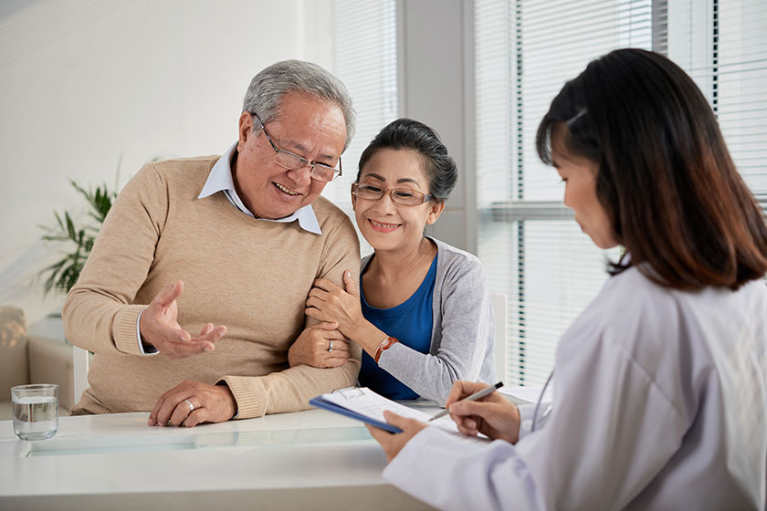 Happy senior Vietnamese couple signing contract with insurance agent