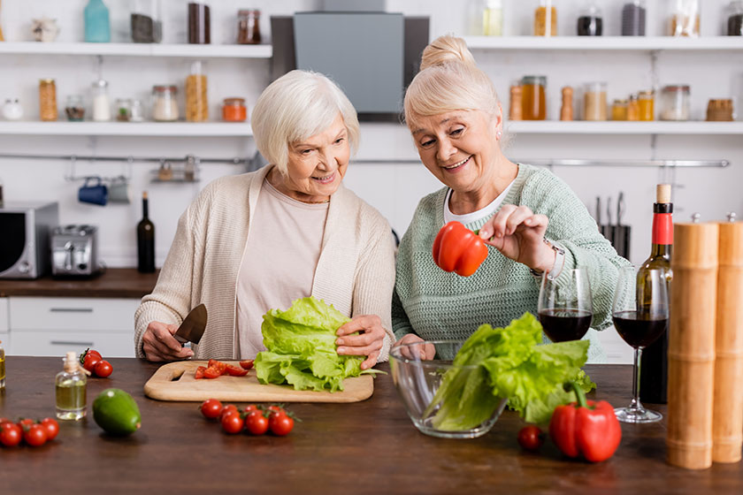 Happy senior woman looking at fresh bell pepper with retired friend