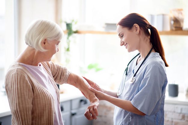 Caregiver putting gel on elbow of retired woman Caregiver putting gel on elbow of retired woman