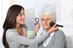 Young woman helping old woman to put makeup on