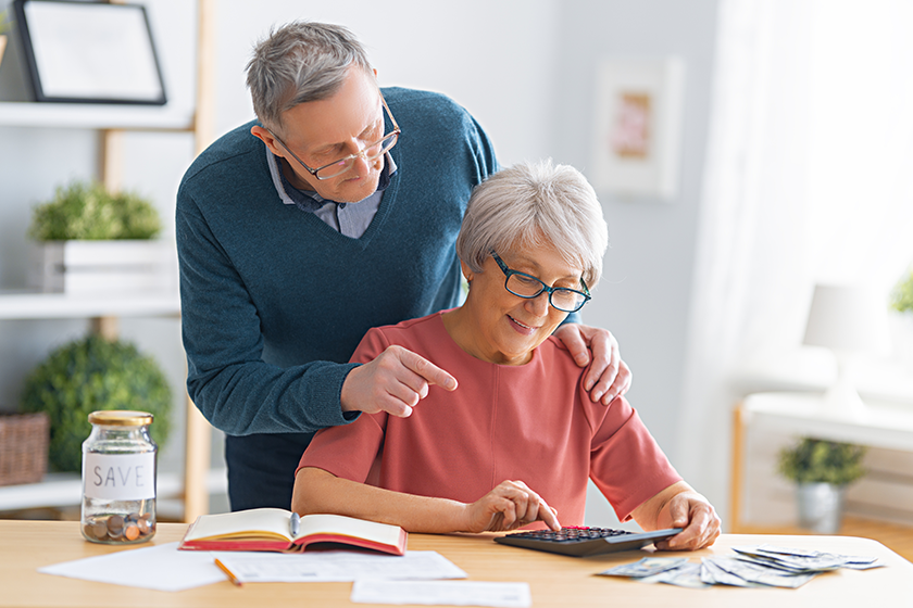 elderly married couple sitting desk paper receipt hands calculating expenses