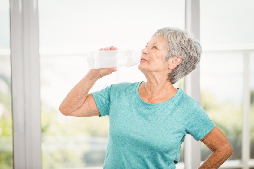 Senior woman drinking water while exercising at home