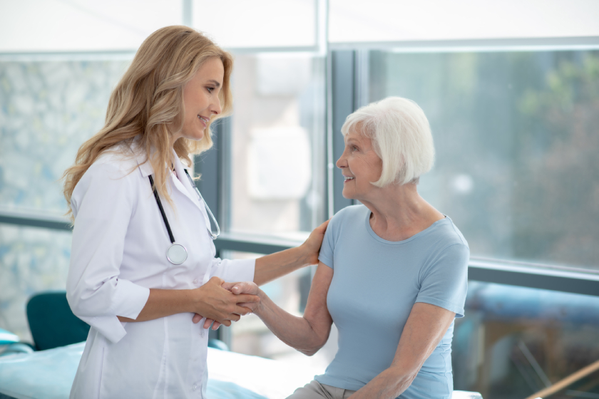 Long-haired cute smiling nurse talking to an elderly patient
