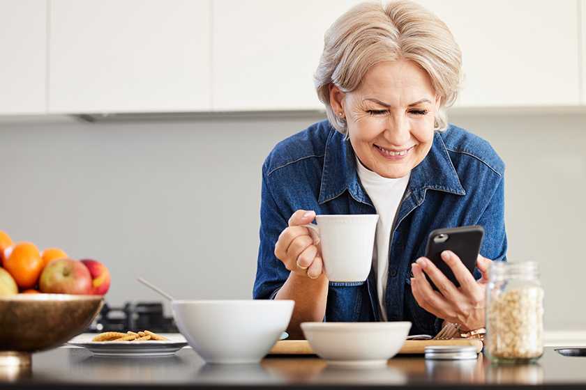 a senior woman using her cellphone and drinking coffee