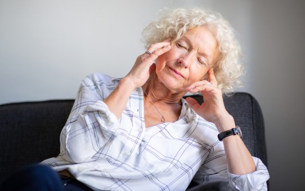 elderly woman sitting on sofa with headache and hands to head Making Healthy Food Choices For Your Loved Ones: How A Senior Living Facility In Webster, TX Can Help