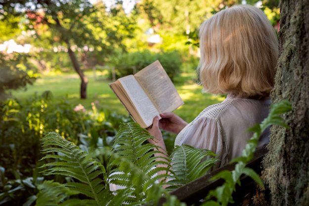 Senior woman in summer garden reading a book